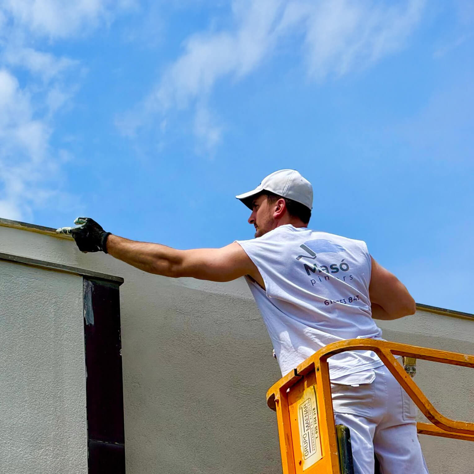 Pintor professional de Masó Pintors treballant en alçada, aplicant pintura blanca al remat d'una façana exterior de to clar, amb un acabat net i d'alta qualitat.